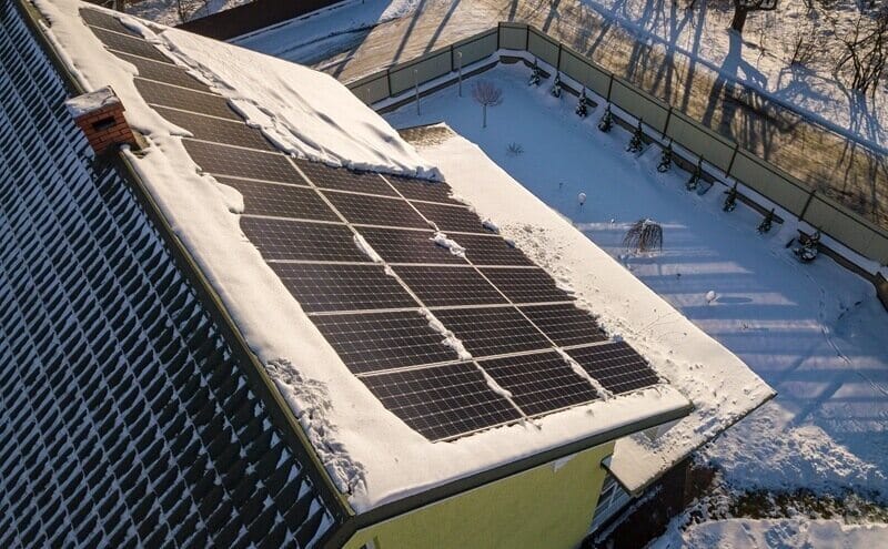 close up surface of a house roof covered with solar panels in winter with snow on top